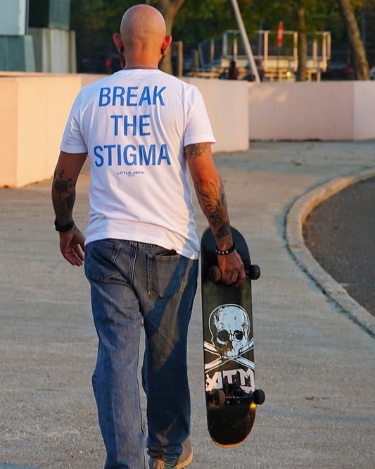 Person walking with a skateboard, wearing a white shirt with 'BREAK THE STIGMA' written on the back.