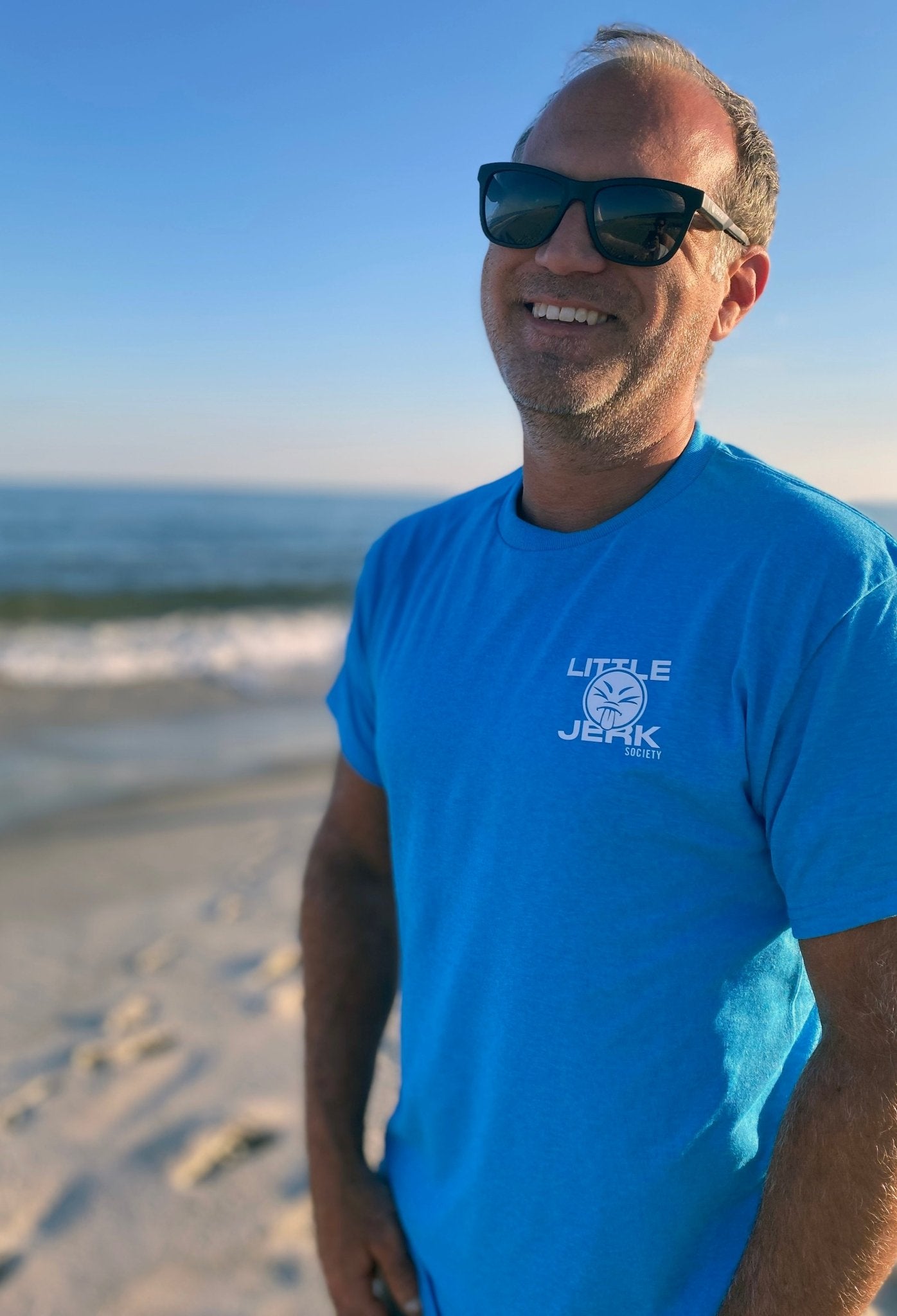 Smiling man wearing sunglasses and a blue t-shirt standing on the beach