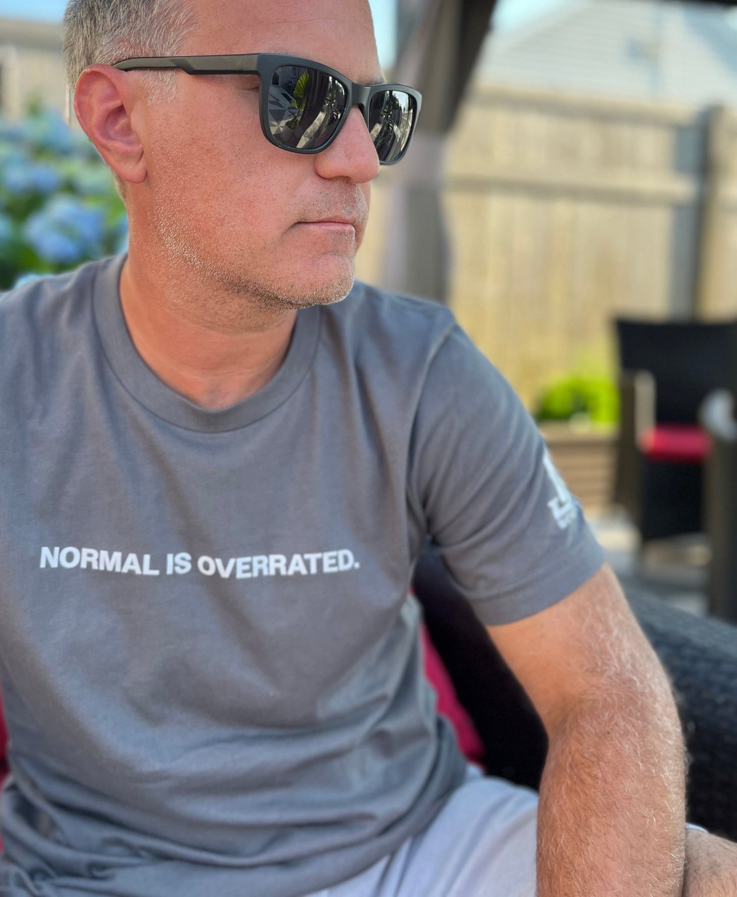 Person wearing a gray t-shirt with the text 'NORMAL IS OVERRATED.' and sunglasses.