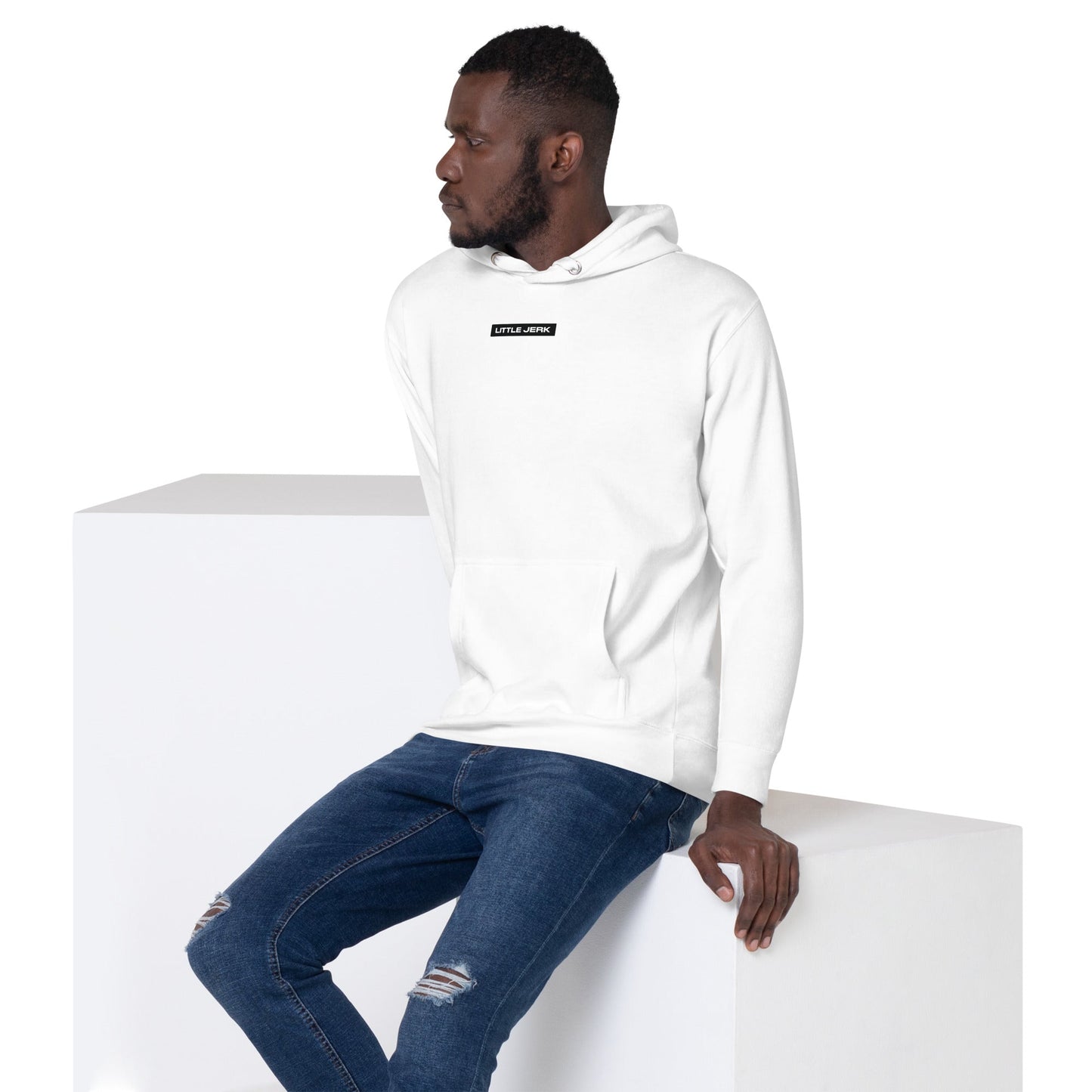 A man wearing a white hoodie and jeans, seated on a white pedestal.