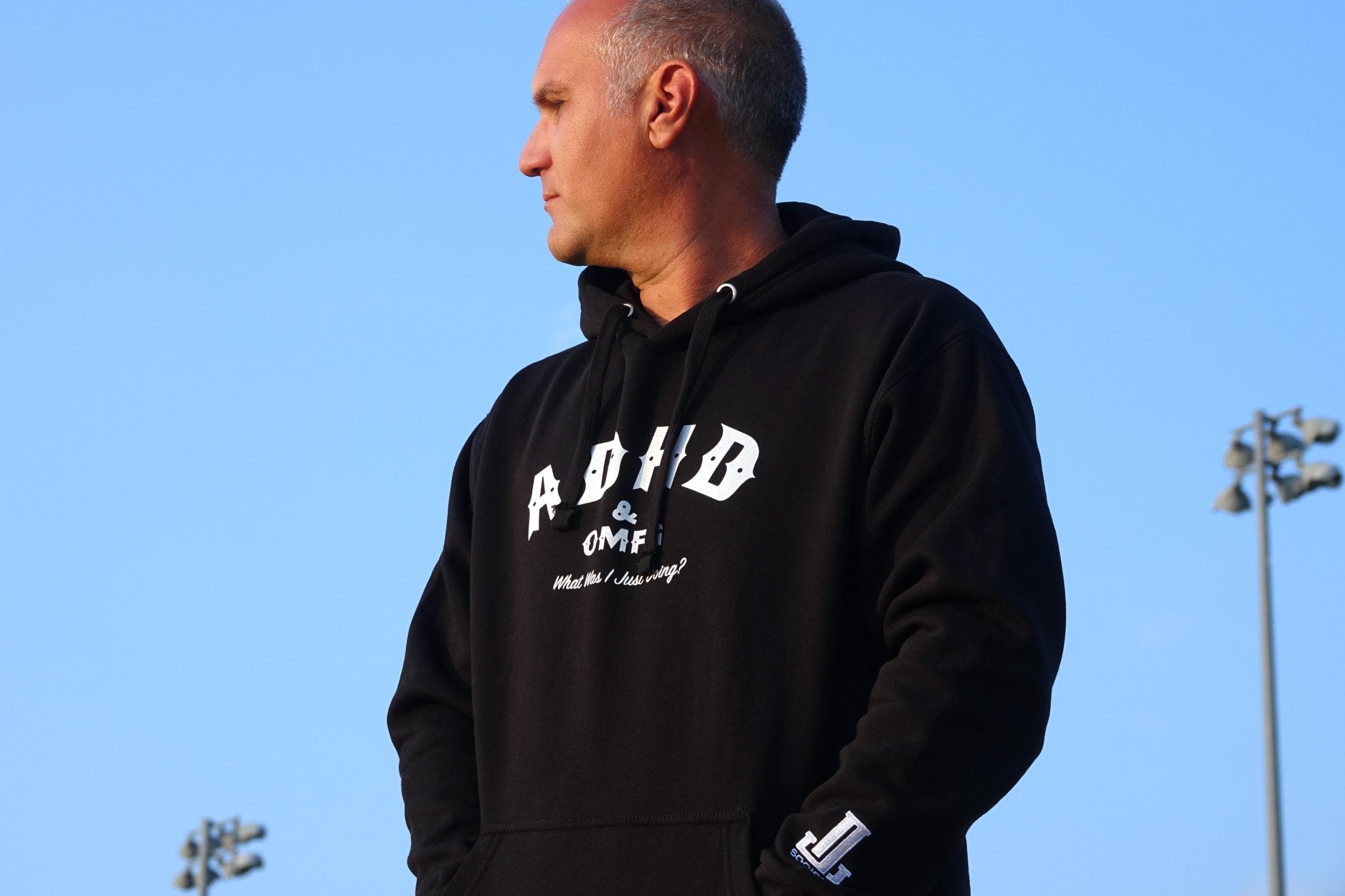 Person wearing a black hoodie standing outdoors with a blue sky background.