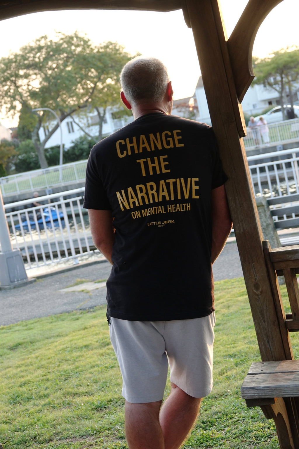 Person standing outdoors wearing a t-shirt with the message 'CHANGE THE NARRATIVE ON MENTAL HEALTH' on the back.